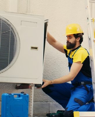 Professional worker starting work on malfunctioning air conditioner, using power drill to take apart condenser side coil panel. Capable electrician dismantling hvac system to check for faulty wires